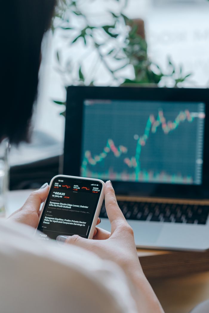 gallery-3 Person using smartphone for stock market analysis at home office.