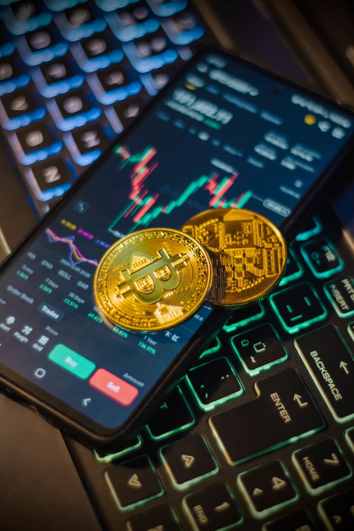 hero-img-01 Cryptocurrency trading interface on a mobile with Bitcoin coins on a laptop keyboard.